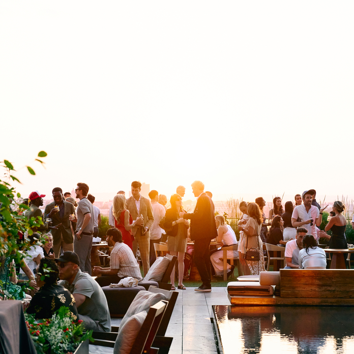 People enjoying a sunset on a rooftop at a restaurant with a pool and seating.